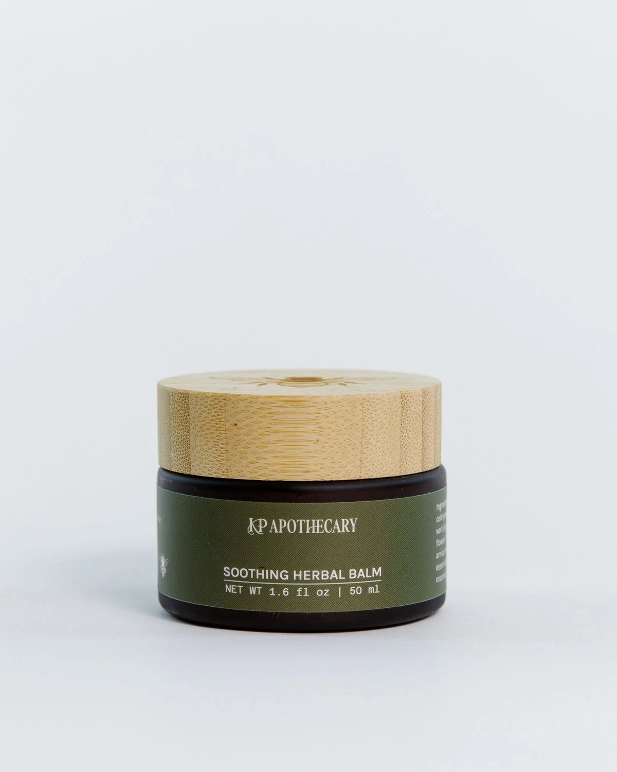 KP Apothecary Soothing Herbal Balm in a dark olive green jar with a light bamboo lid, set against a clean white background.